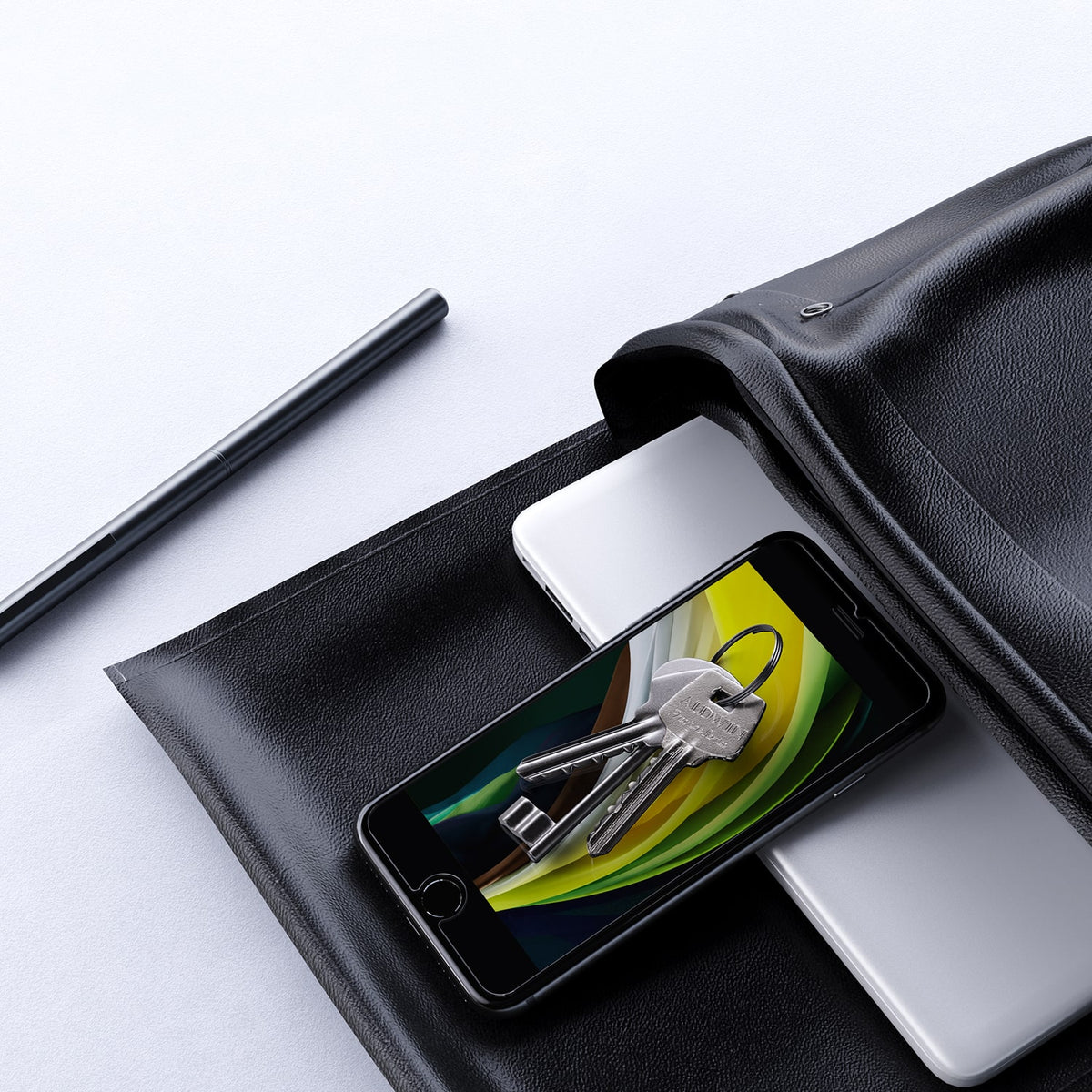 a black office bag with a computer, keys, a pen, and an iphone with unrbeakcable screen protector on